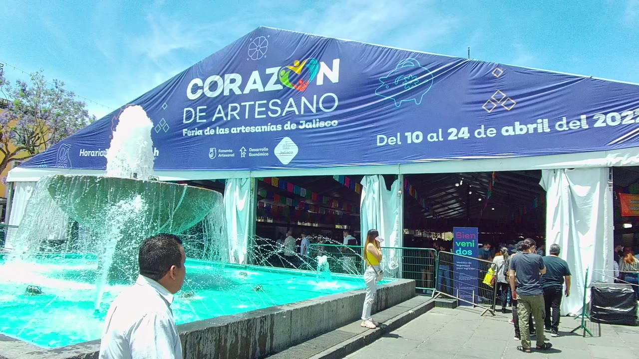 Man in white shirt passes the fountain with the artisan fair tent behind him.