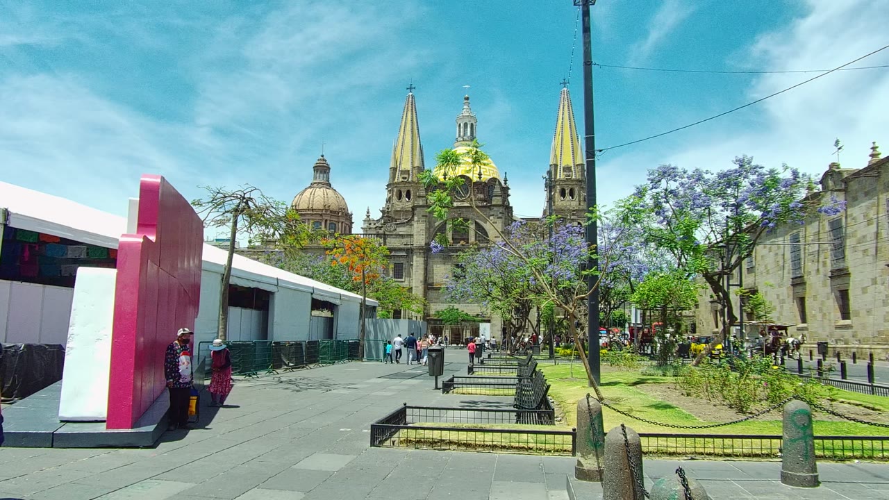 Pedestrians move through a paved square near a cathedral and pink structure.