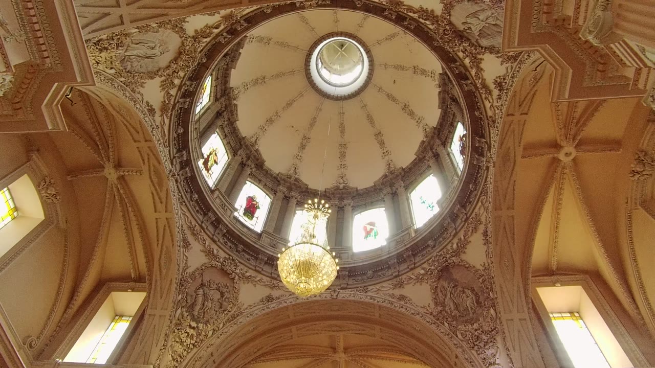 Decorated dome ceiling with chandelier and bright window openings.