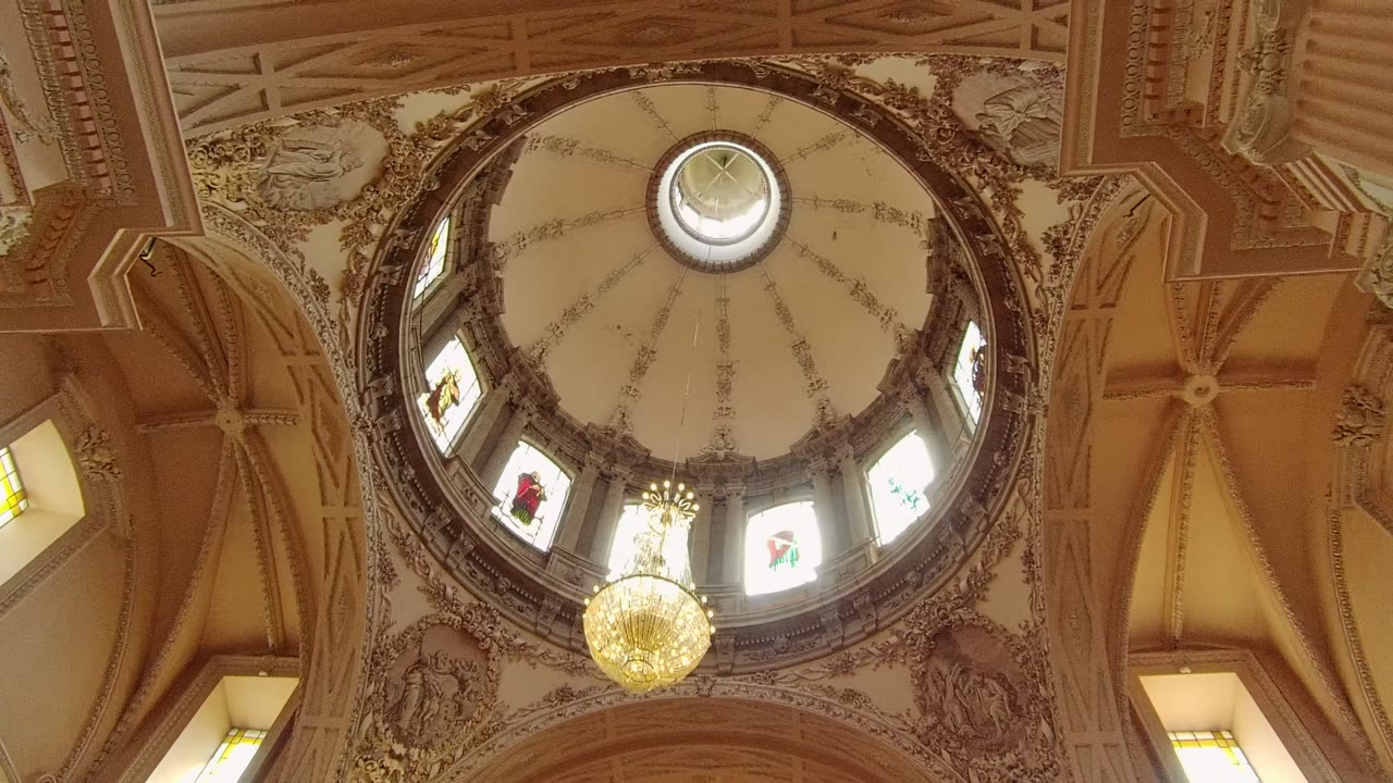 Near-centered view of the Guadalajara dome ceiling, with the chandelier hanging below the window ring and no visible people in the interior frame.