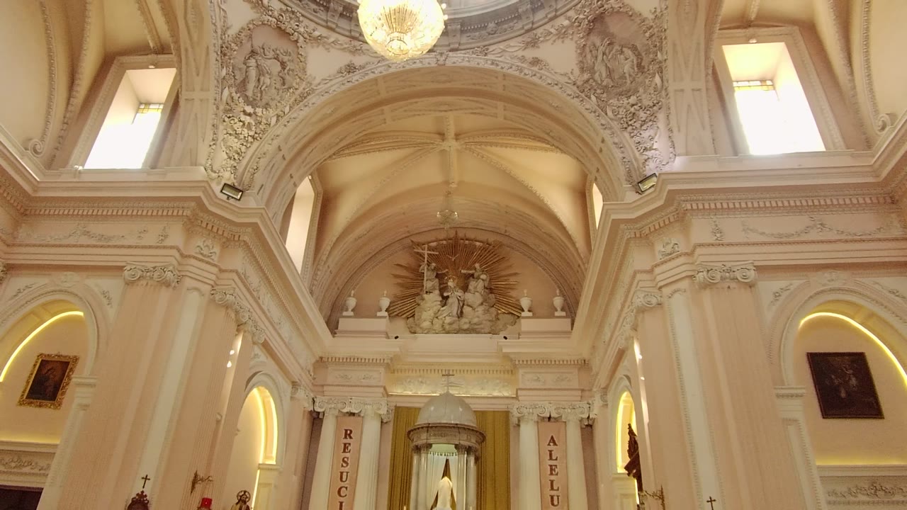 Upward view inside a Guadalajara, Mexico church showing cream arches, carved ornament, stained glass windows, a gold chandelier, and no visible people.