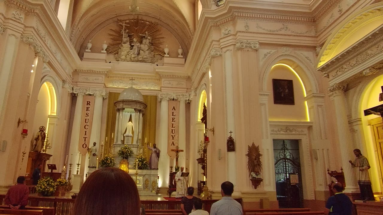 A Guadalajara church interior faces the altar with vertical religious banners, statues, floral arrangements, and seated visitors seen from behind in the pews.