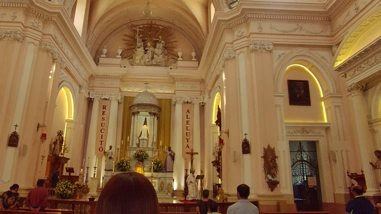 White church interior with altar, banners, arches, and visitors in pews.