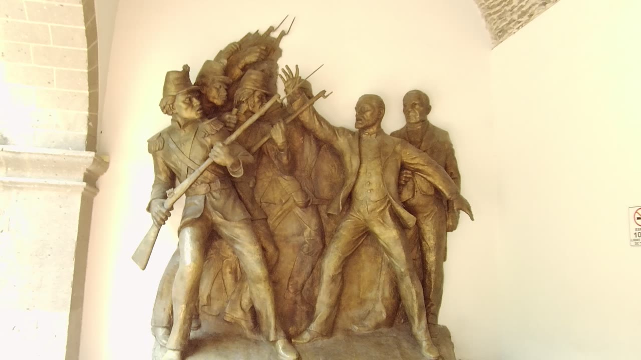 Bronze figures and rifle sculpture beside a stone column.