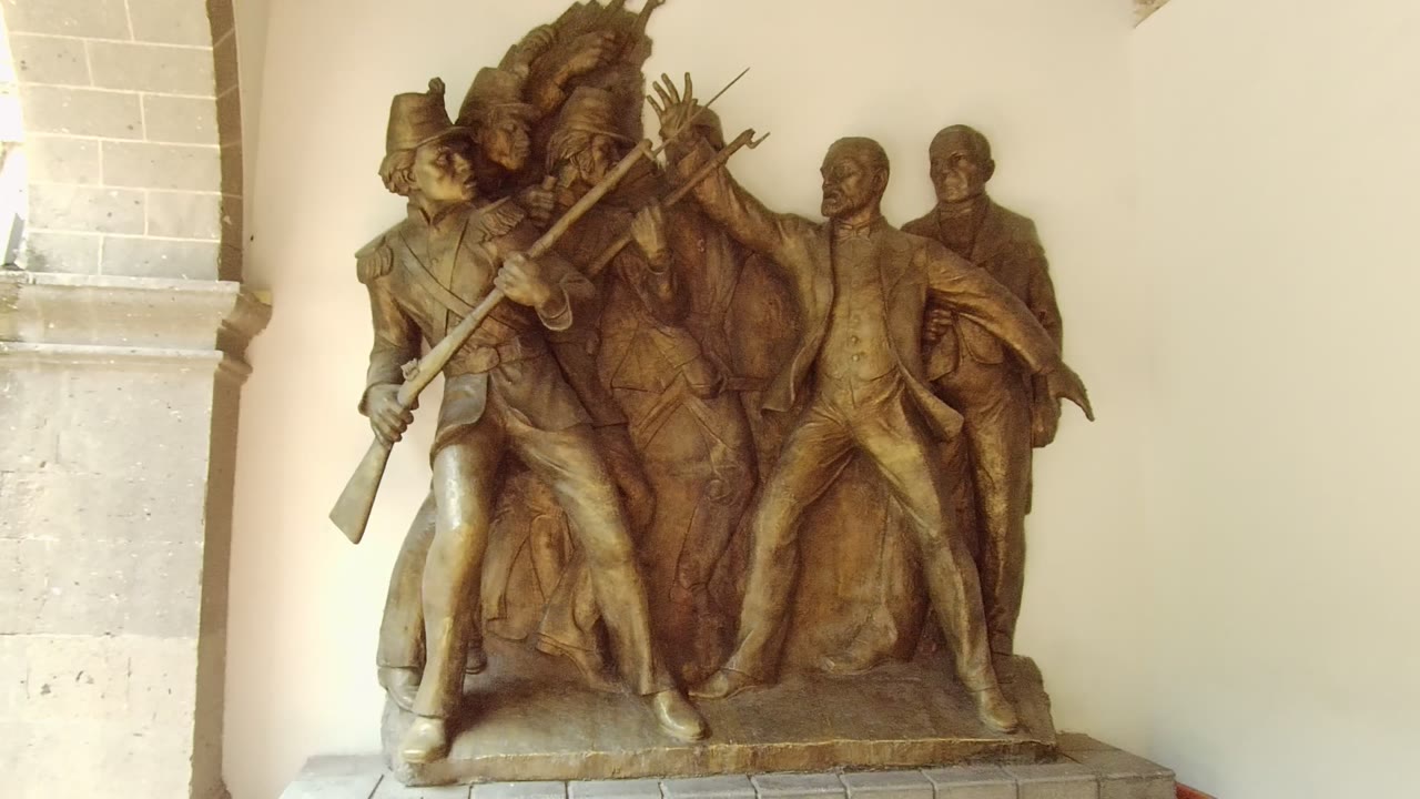 A wider view in Guadalajara, Mexico shows the bronze relief on its stone base, with arched masonry above, a pale wall behind, and no visible people.