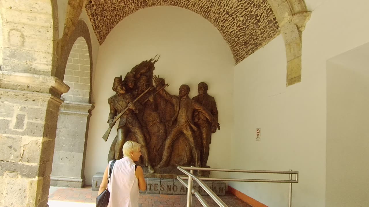 Girl in pink walking past bronze wall relief