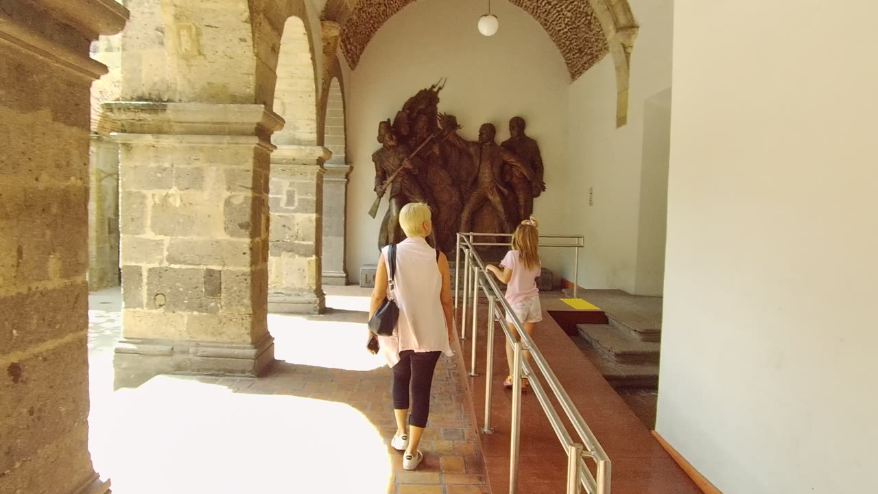 Woman and child continuing toward a large statue in an arched courtyard.