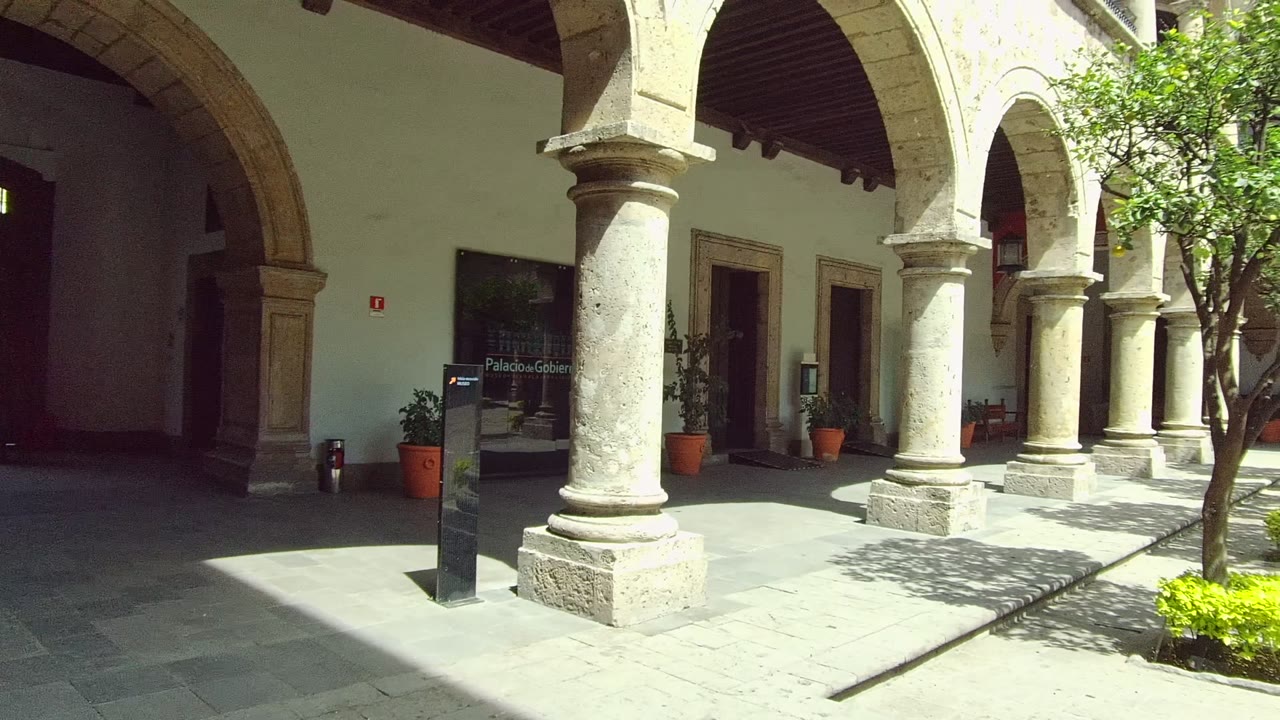 Arched courtyard walkway with columns, plants, and tree shadows