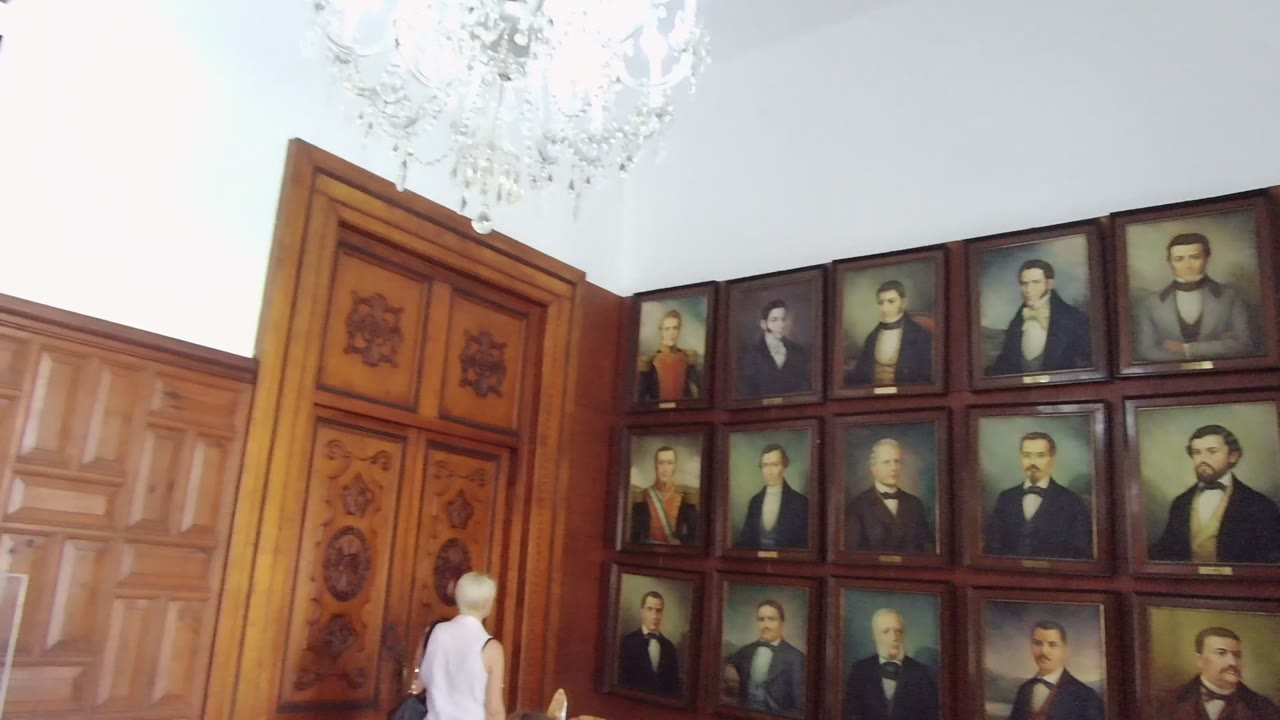 Carved wooden door beside rows of framed portraits with a person below.