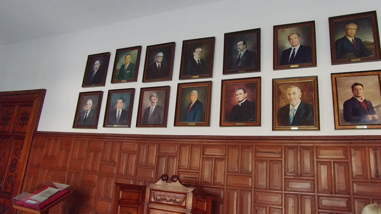 Rows of framed portraits on a white wall above carved wooden wainscoting and a lectern area.