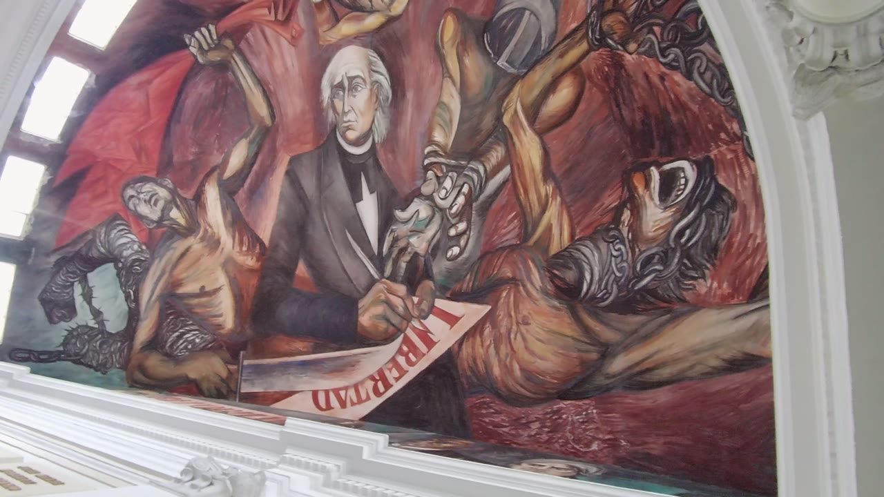 Guadalajara mural detail at 0:00 showing a suited historical figure holding a Liberty document, surrounded by painted allegorical figures and red-brown background tones, with no visible live people.
