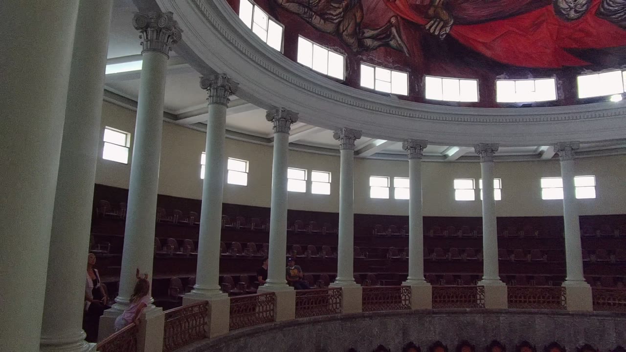 Domed hall interior with columns, balcony rail, bright windows, and red ceiling mural.