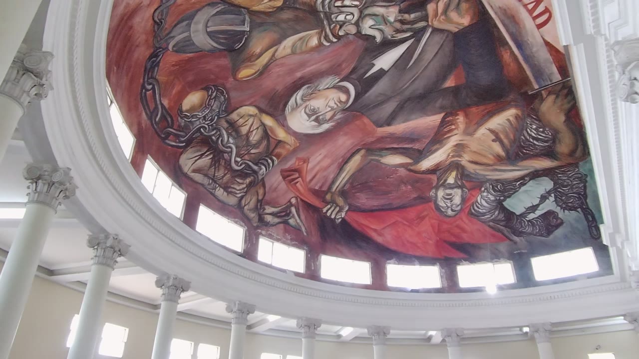 Opening frame of a Guadalajara dome interior showing the red mural, painted figures, white columns, bright windows, and no visible people.