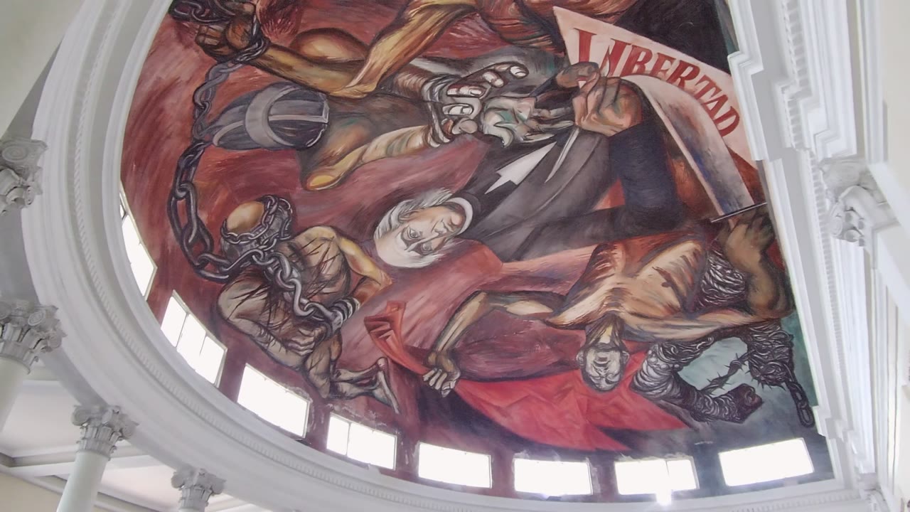 Mid-clip frame from the Guadalajara interior shows the LIBERTAD banner entering near the right side above the red mural and no visible people.
