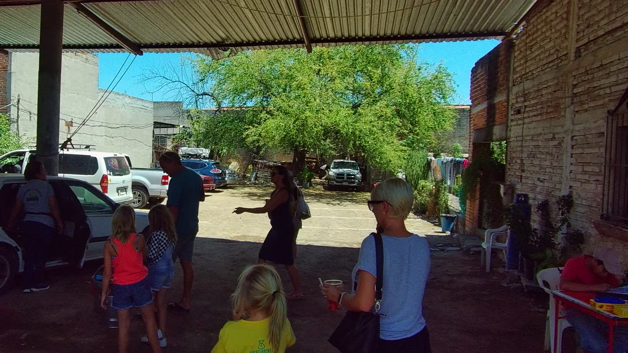 Group moving through a carport with a white vehicle and trees behind them.
