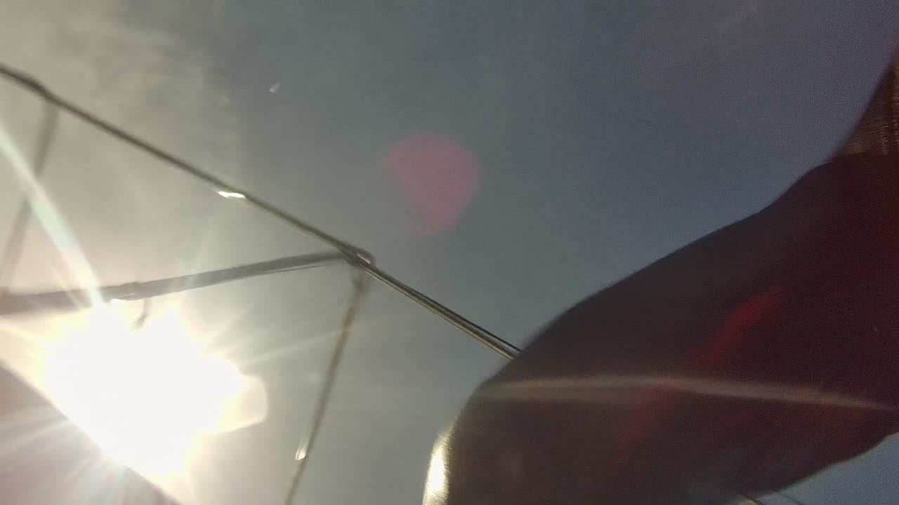 At Cabo Pulmo, Baja California Sur, bright sun flares near sailboat rigging while a dark sail and hull edge sit close to the water, with no visible people.