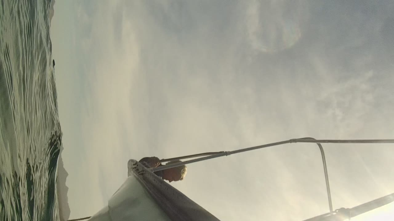 Close sailboat hull and rigging seen from the water with pale sky behind it.