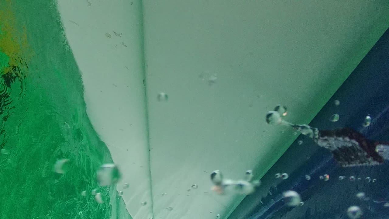At Cabo Pulmo, the frame shifts underwater beside the hull, showing green-blue water, bubbles, and the underside of the boat with no visible people.