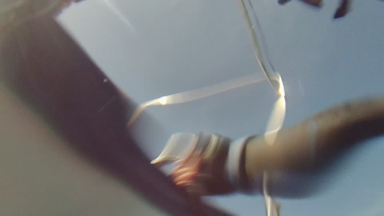 Low-angle view from a sailboat deck in Cabo Pulmo, with blurred arms, a rope, rigging, and bright pale sky filling the frame.