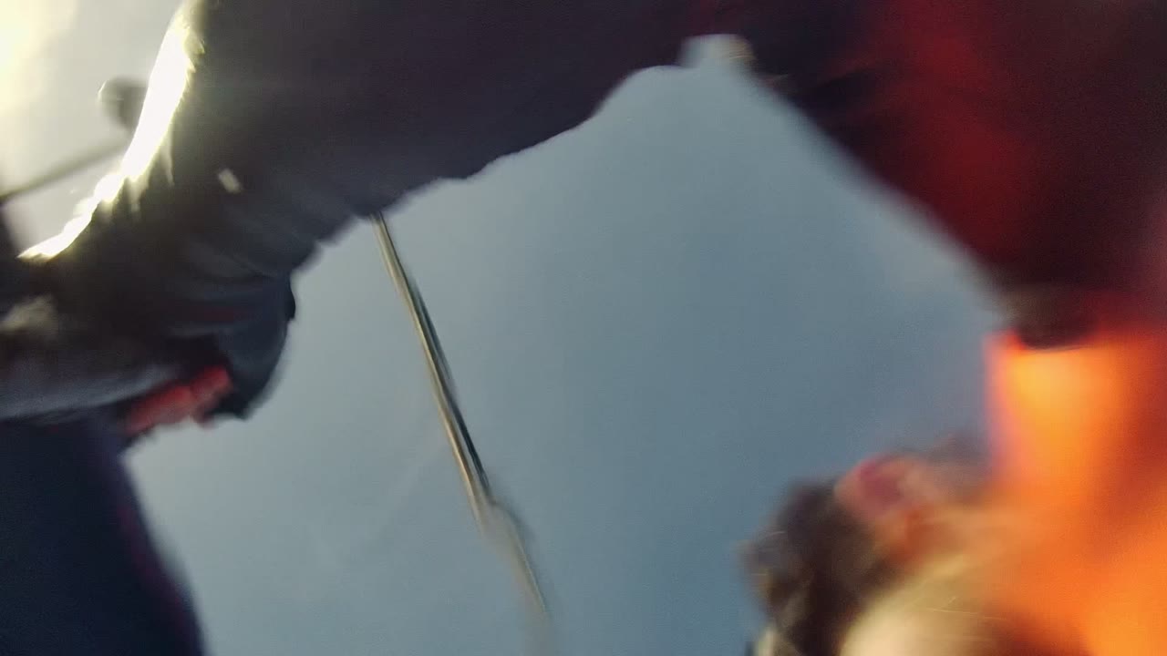 Person and gear blurred close to the lens against sky and sailboat hardware.