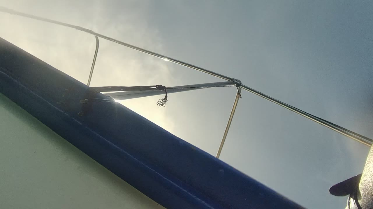 A dark sailboat rail or boom crosses the frame in Cabo Pulmo, with metal rigging lines silhouetted against bright sun and pale sky and no visible people.
