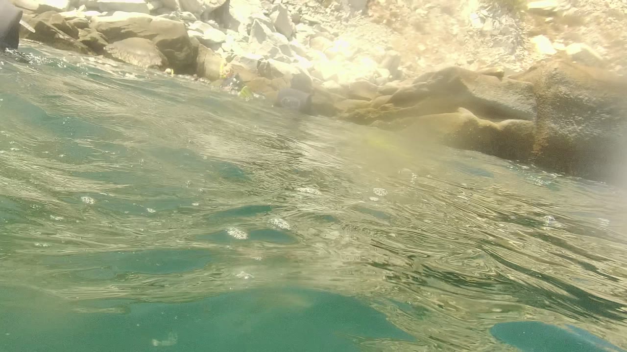 Rippling water surface with pale rocks along the upper edge and no visible people.