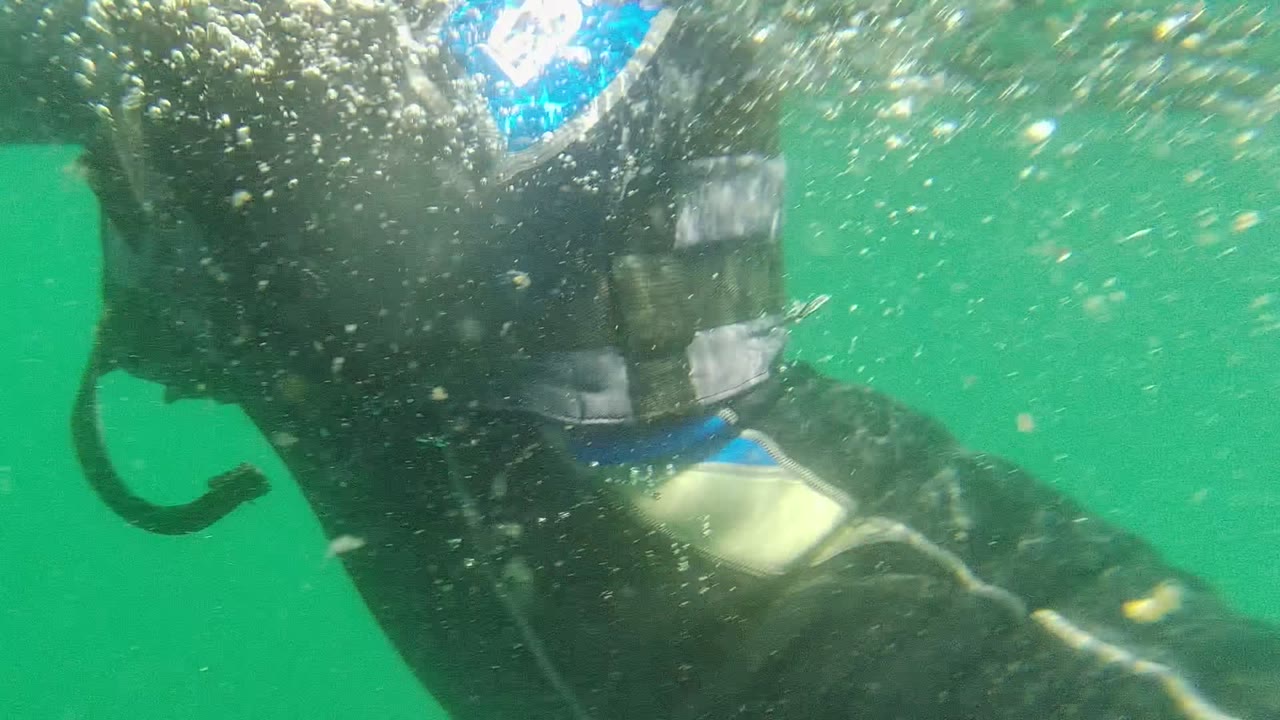 Close underwater frame from Cabo Pulmo showing a wetsuited scuba diver and gear near the lens in green water, with bubbles and no clearly visible face.