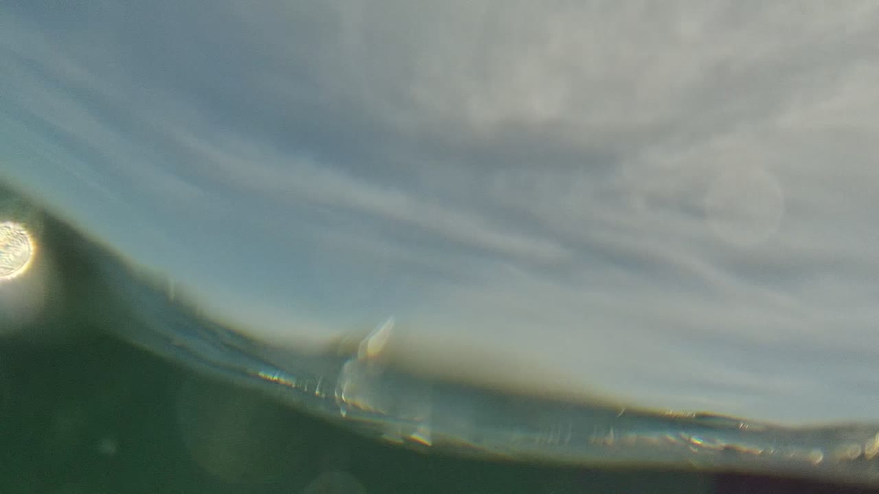 Underwater view in Cabo Pulmo looking up at a rippled water surface with pale sky, blurred sun glints, green water, and no visible people.