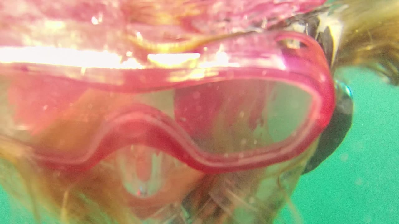 Close underwater view in Cabo Pulmo, Mexico, showing a snorkeler's pink mask and hair near the rippled water surface.