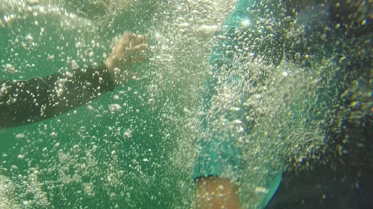 Dense bubbles and foam fill the foreground as a partially visible swimmer moves through the turquoise water in Cabo Pulmo.