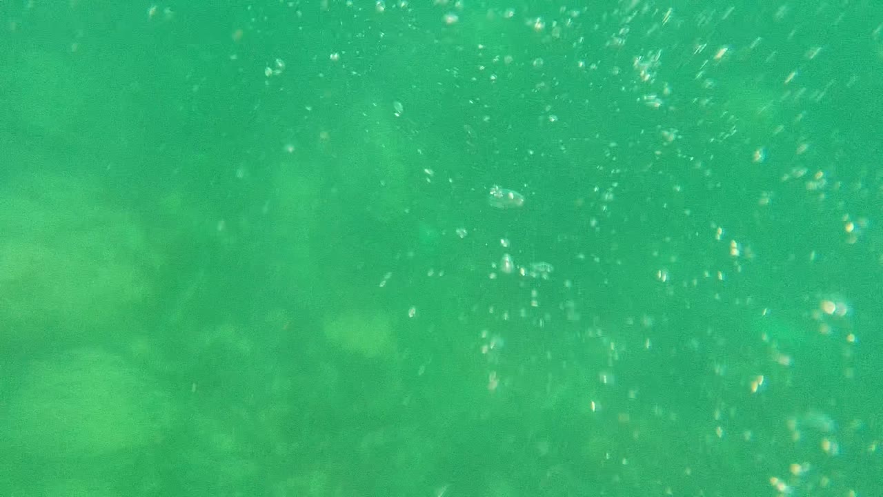 Bubbles rising through green water above faint seabed rocks