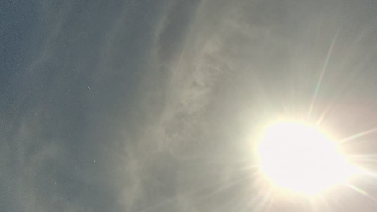 A large sun flare dominates a soft gray water-texture frame from Cabo Pulmo, with no visible people.
