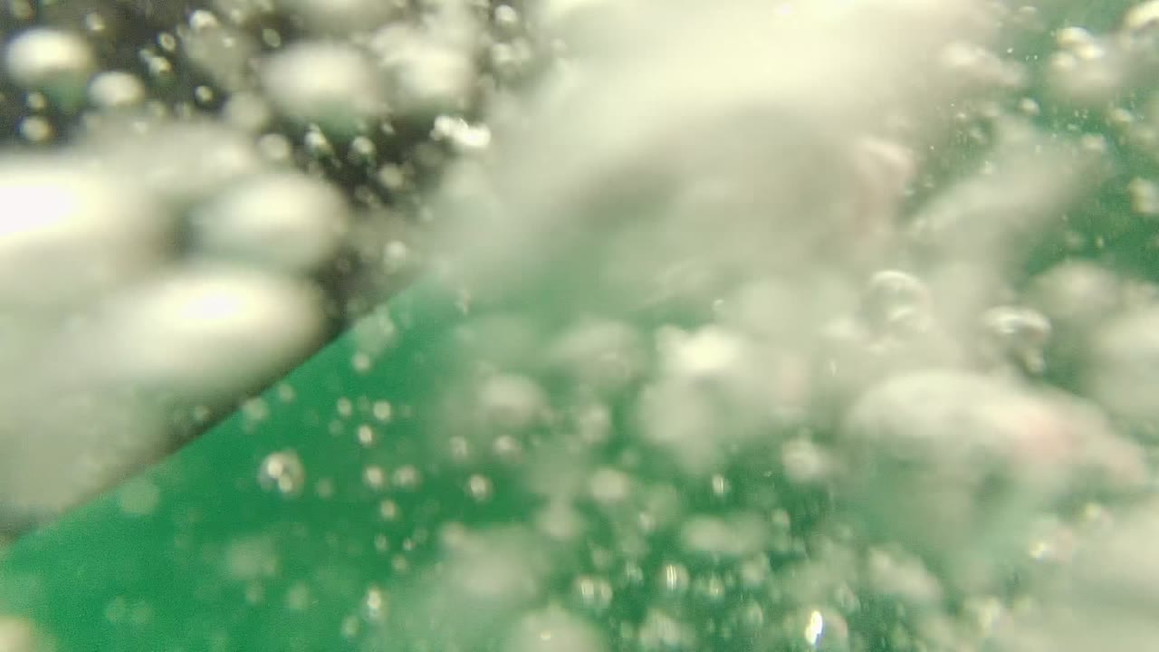 Underwater bubbles and pale foam drift beneath green-blue surface light in Cabo Pulmo, with no visible people.