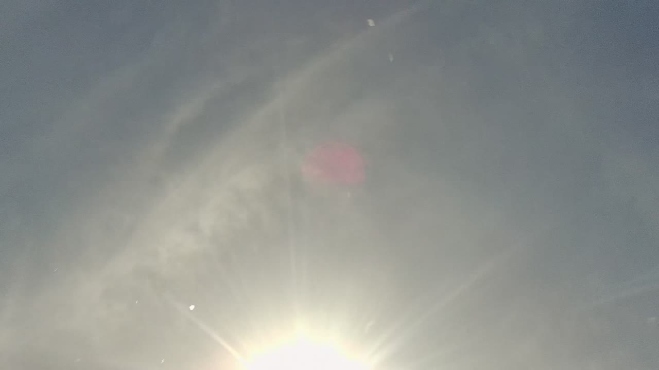 Bright direct sun and lens flare wash across a hazy sky in Cabo Pulmo, Baja California Sur, with soft bokeh circles and no visible people.