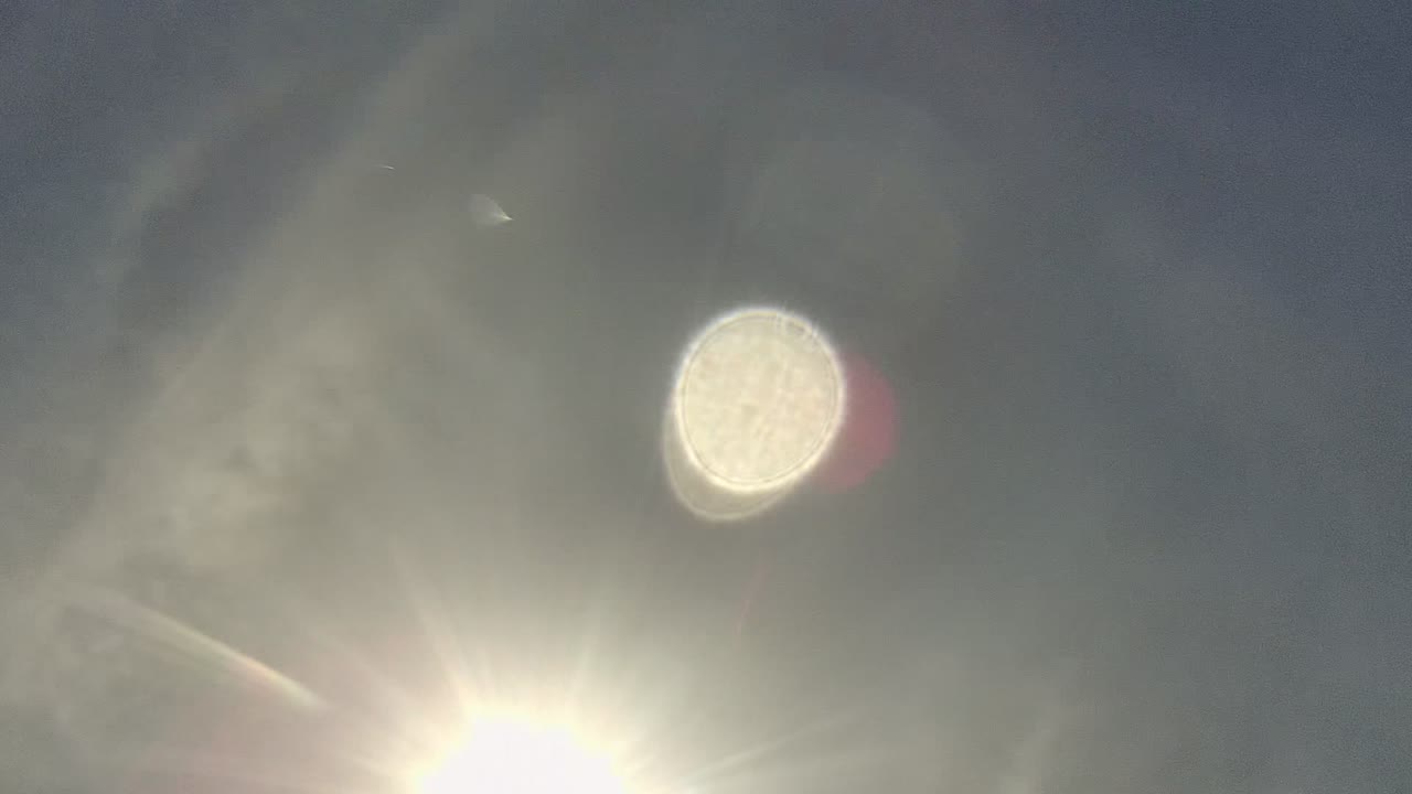 A direct sunburst sits low in a hazy Cabo Pulmo sky while a pale circular flare hovers above it, with no visible people.