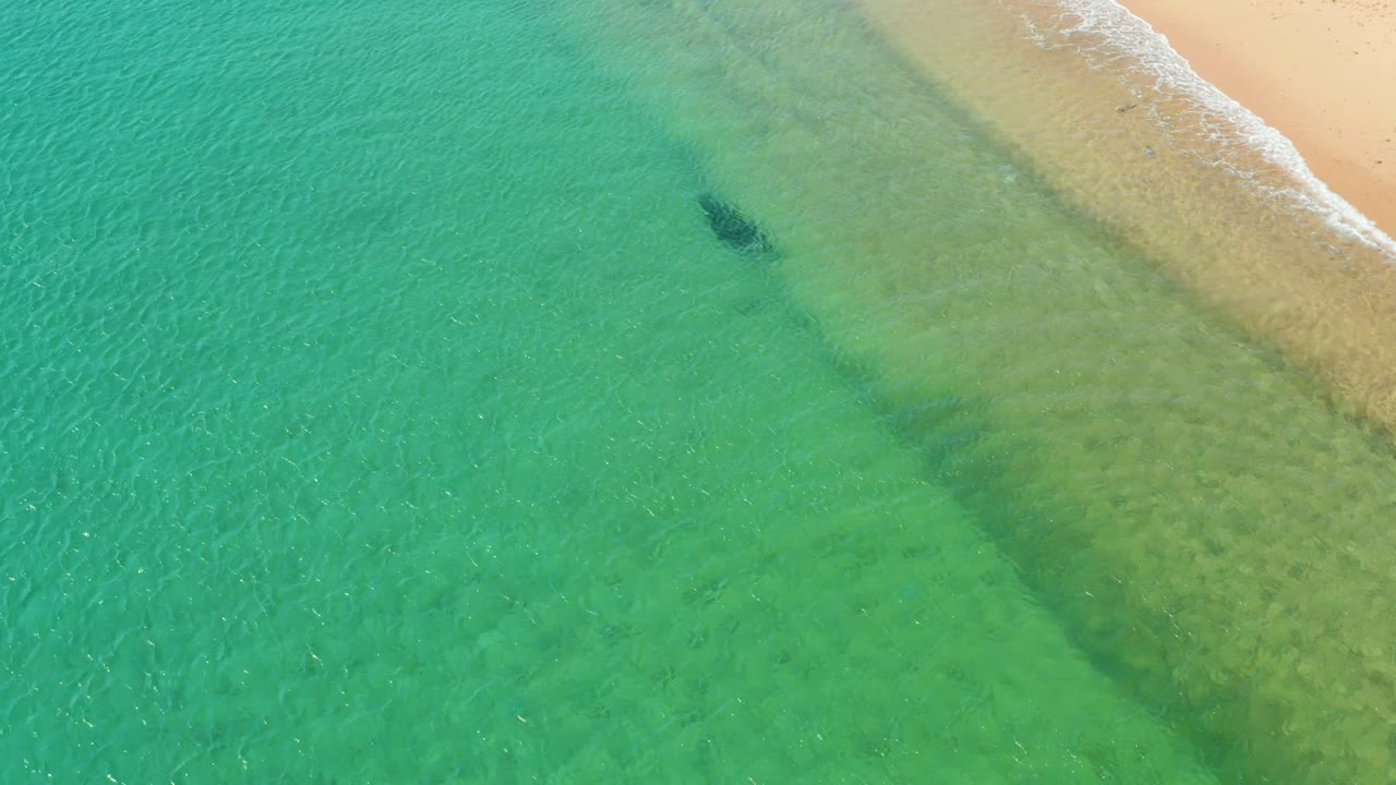 The overhead view shows turquoise water blending into pale green shallows along the sandy Los Frailes shore, with no visible people.