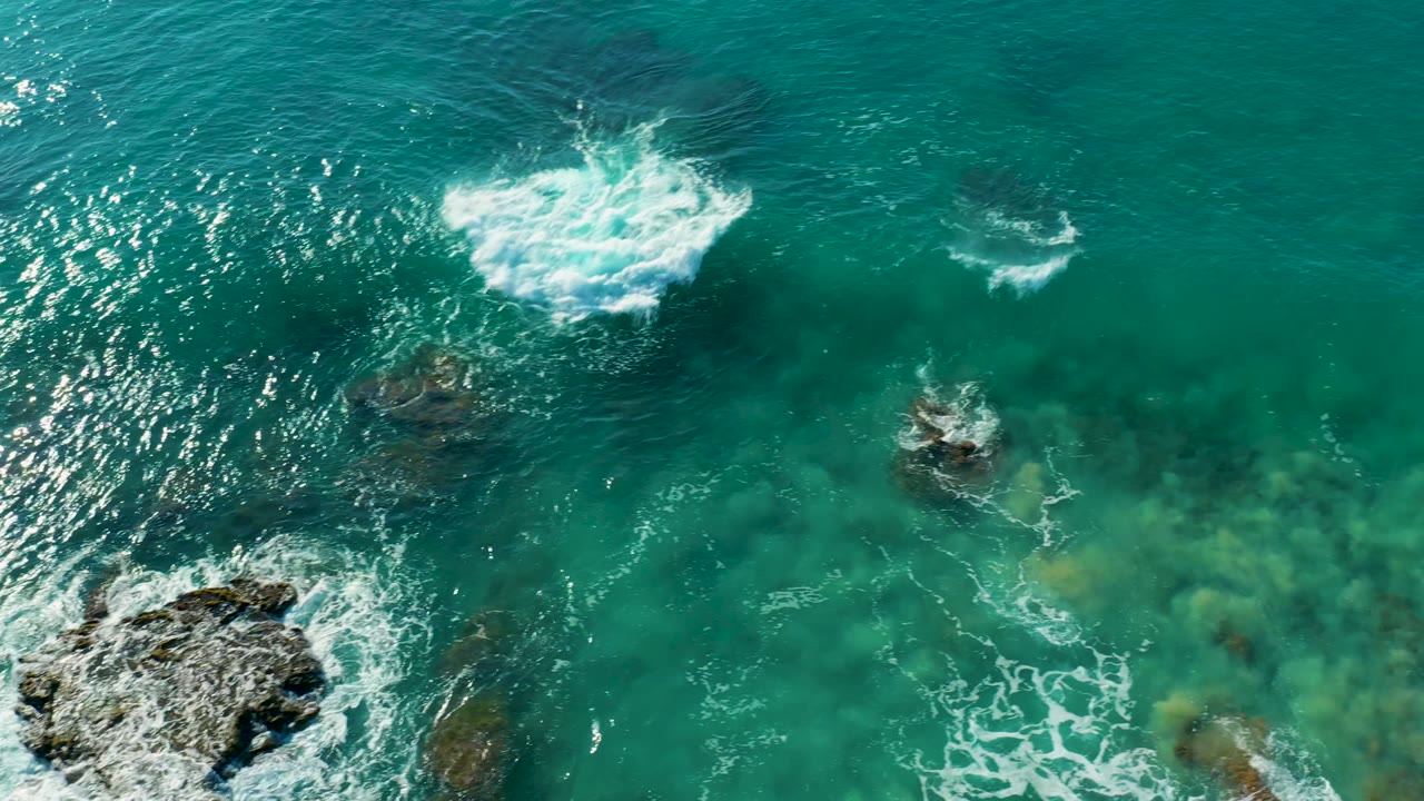 Aerial view of turquoise water at La Fortuna, Baja California Sur, with white surf breaking over submerged rocks and no visible people.