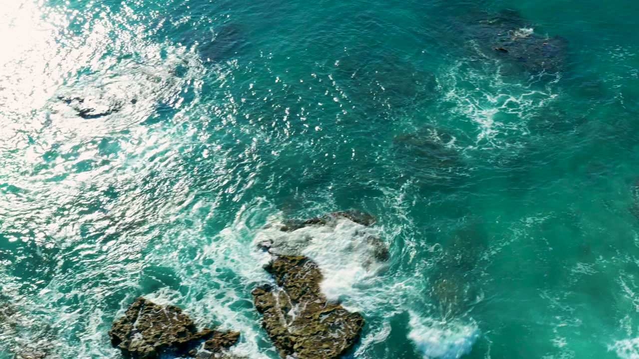 Foam spreading over rocks in clear ocean water