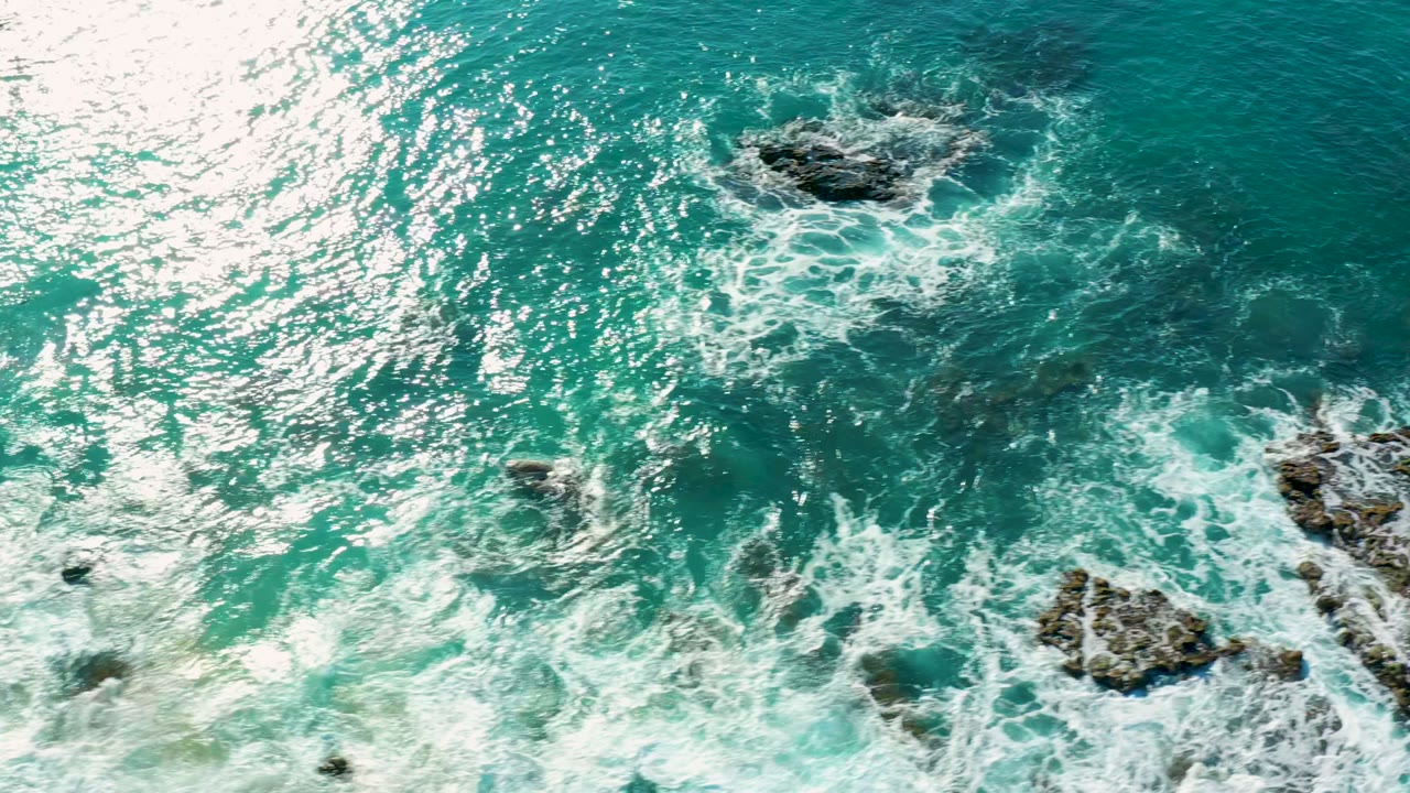 White surf wraps around rocky outcrops in blue-green water.