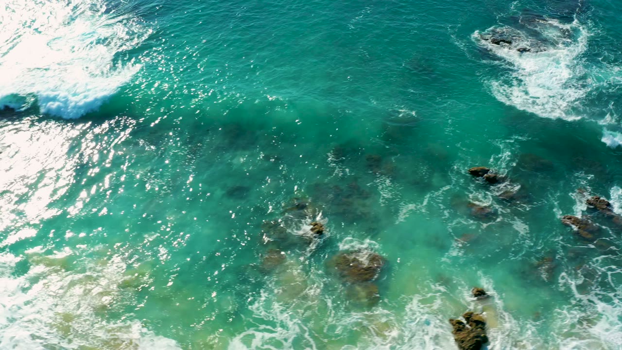 Aerial view of turquoise water and white surf breaking around submerged rocks at La Fortuna, Baja California Sur, Mexico, with no visible people.