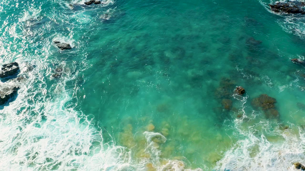 Clear turquoise water with foam breaking over dark submerged rocks.