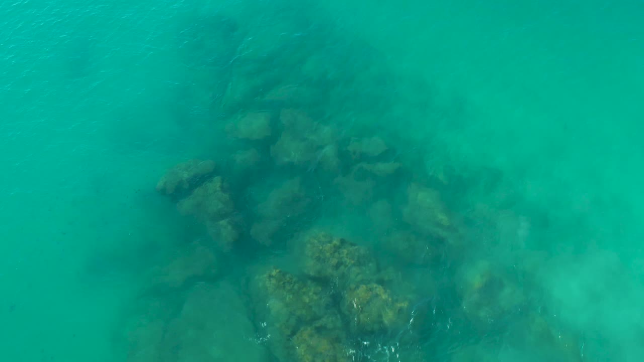 Rocky seabed sits toward the right side of the overhead frame beneath clear turquoise water in La Fortuna, Baja California Sur, with no visible people.