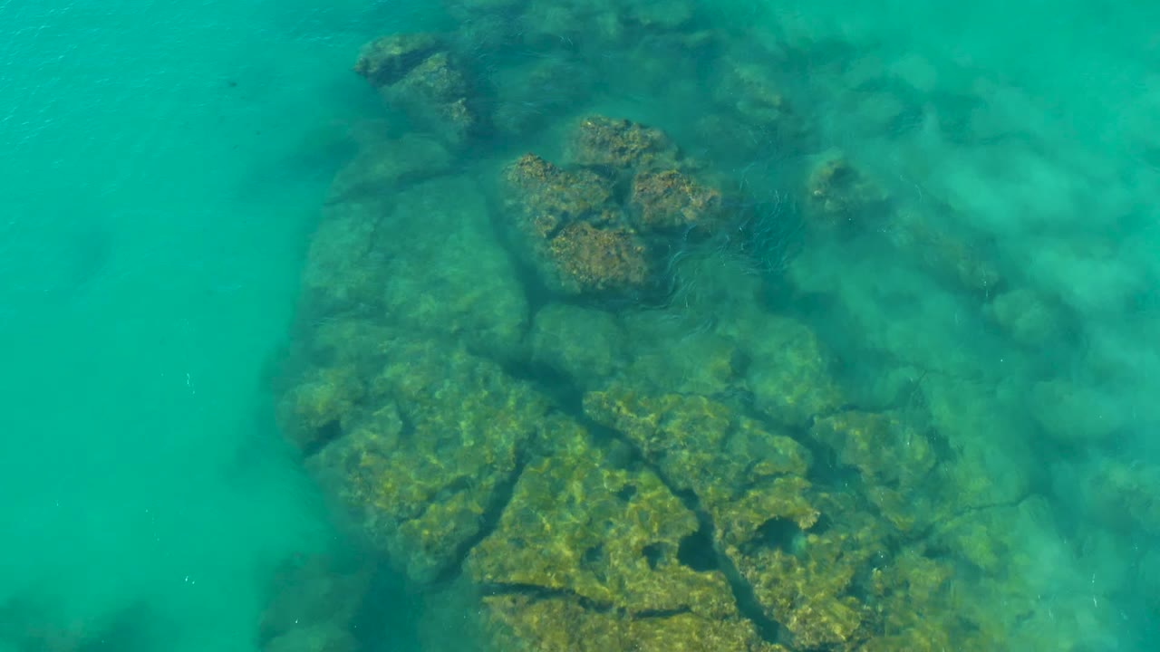 At 0:00, a downward view in La Fortuna, Baja California Sur shows clear turquoise water over large submerged rocks with algae patches and no visible people.
