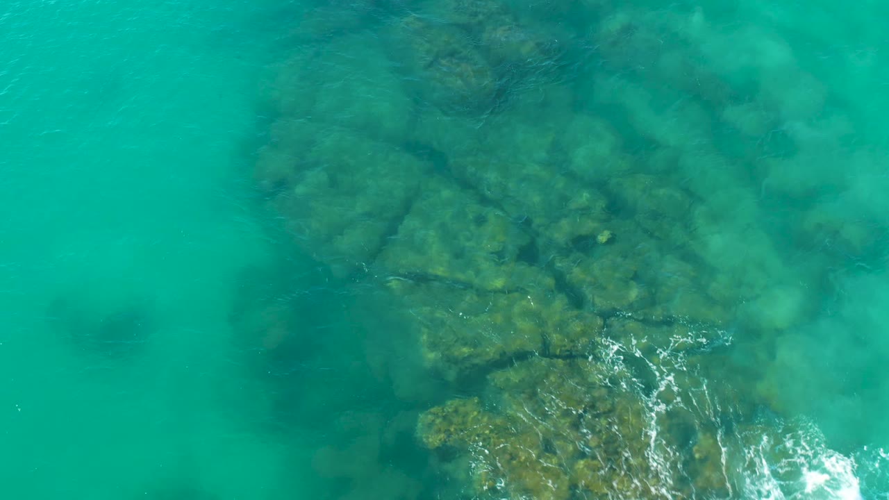 Clear blue-green water over rocky seabed with foam moving near the bottom center.