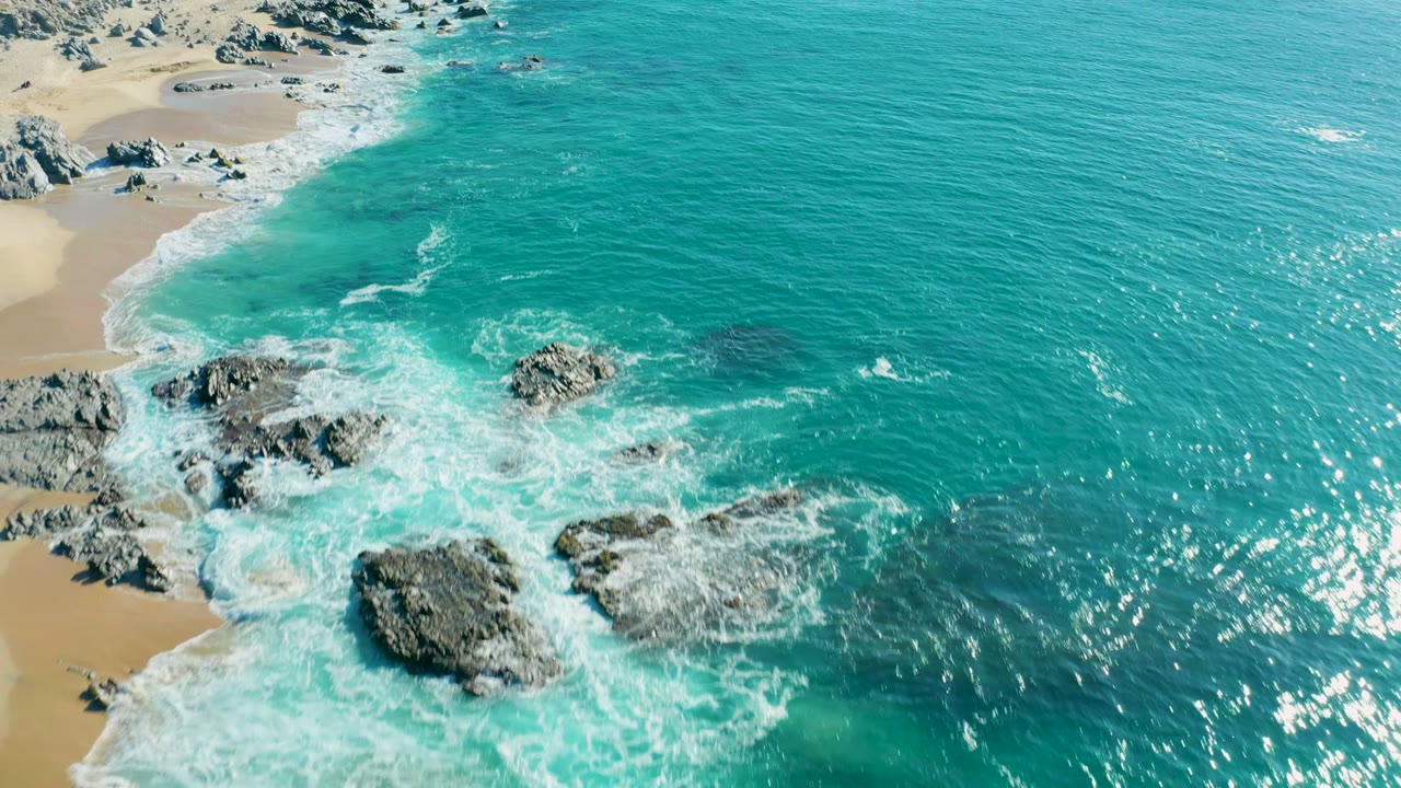 Turquoise ocean and white foam surrounding rocky outcrops near sand