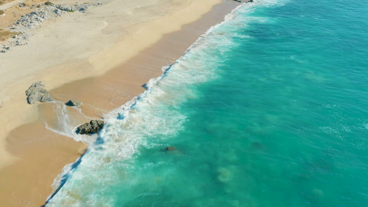 White surf thickens around rocks on a pale sandy shoreline
