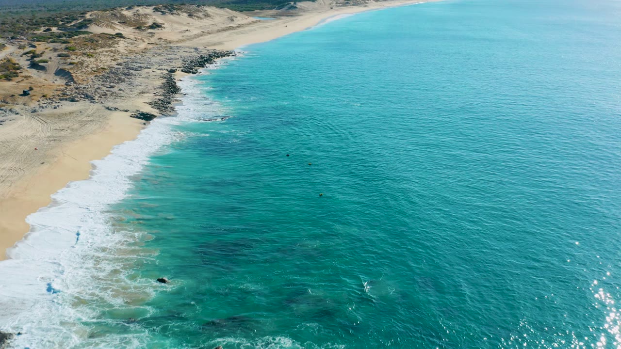 Turquoise ocean and white foam line along a sandy beach seen from above.