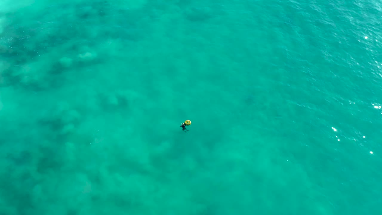 Person floating in clear turquoise ocean with sun reflections nearby.