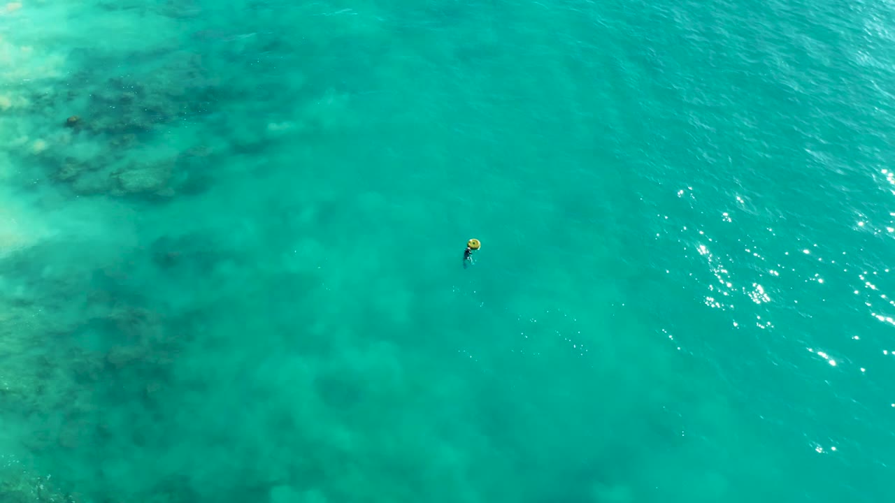 Clear turquoise water with submerged reef texture and a small snorkeler.