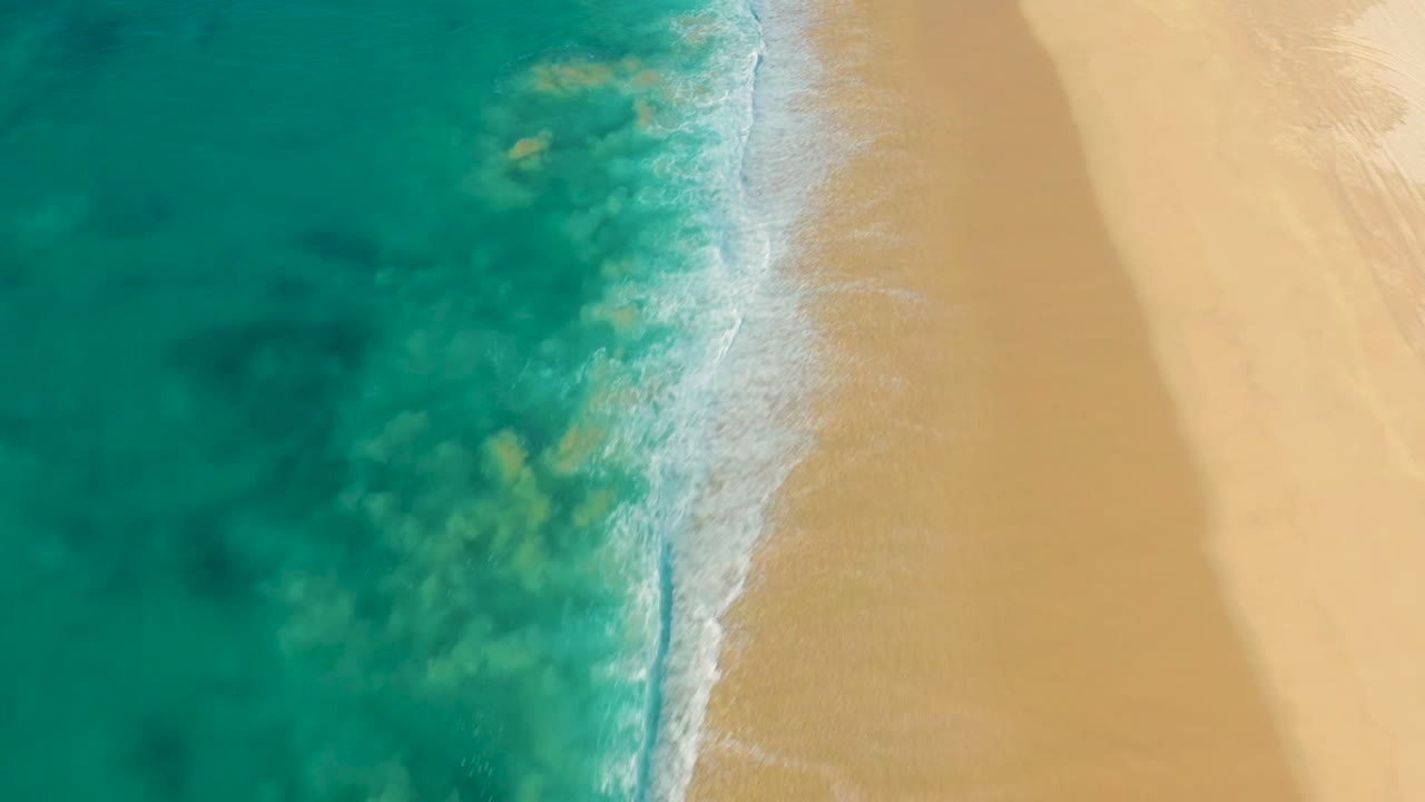 The shoreline narrows into a vertical band of white foam between turquoise sea and empty La Fortuna sand, with no visible people or structures.